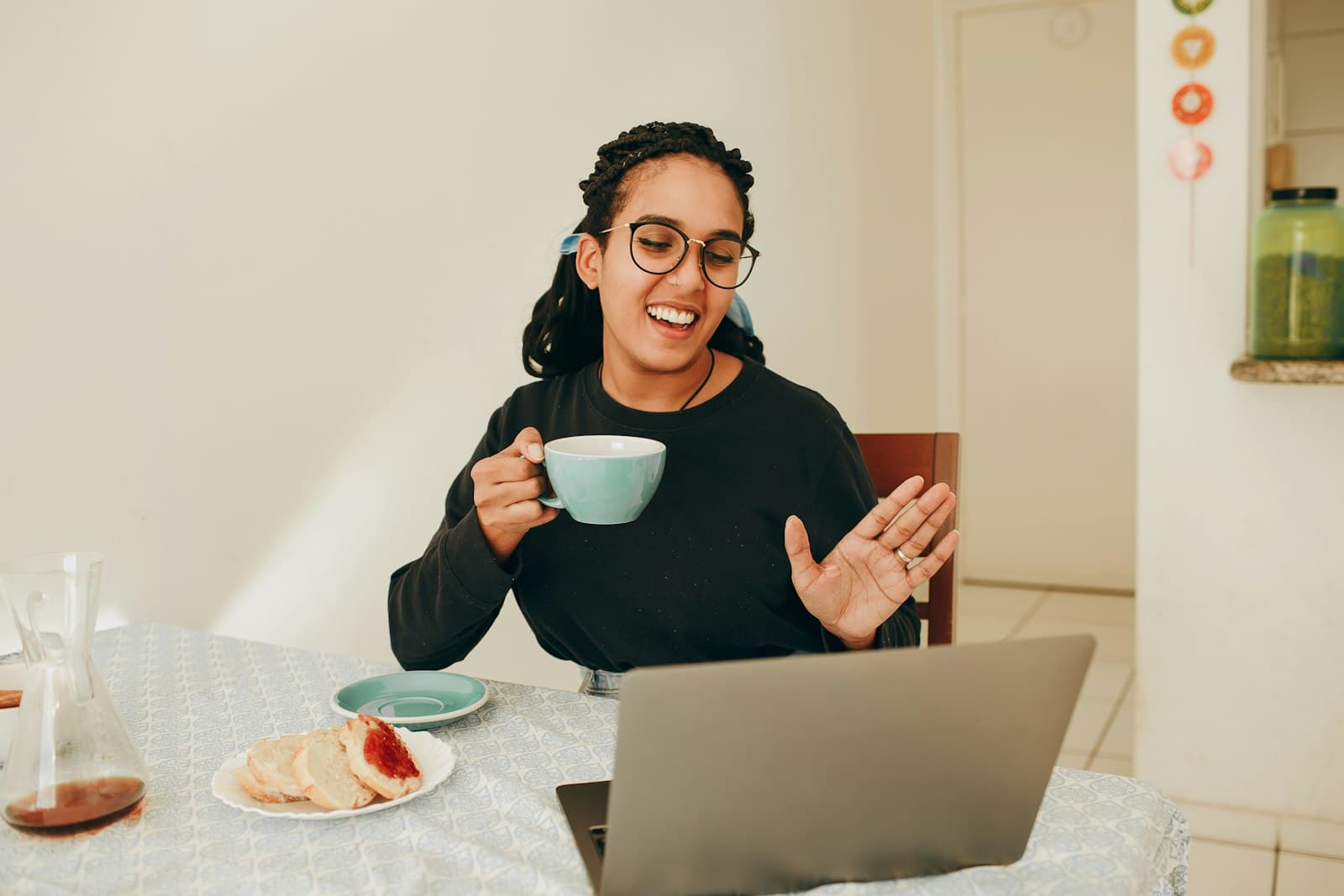 A woman with a coffee waving hello on a video call